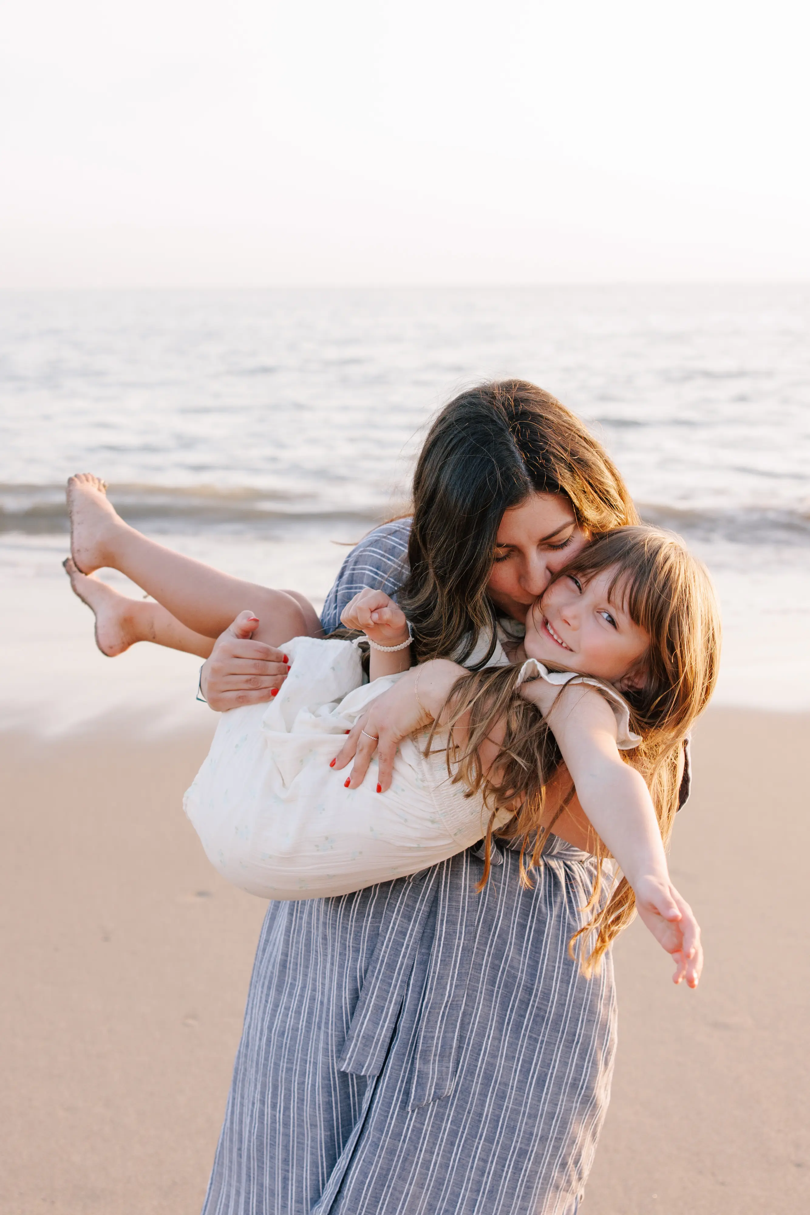 Mother carrying daughter on the beach at golden hour during family photography session in Puerto Vallarta