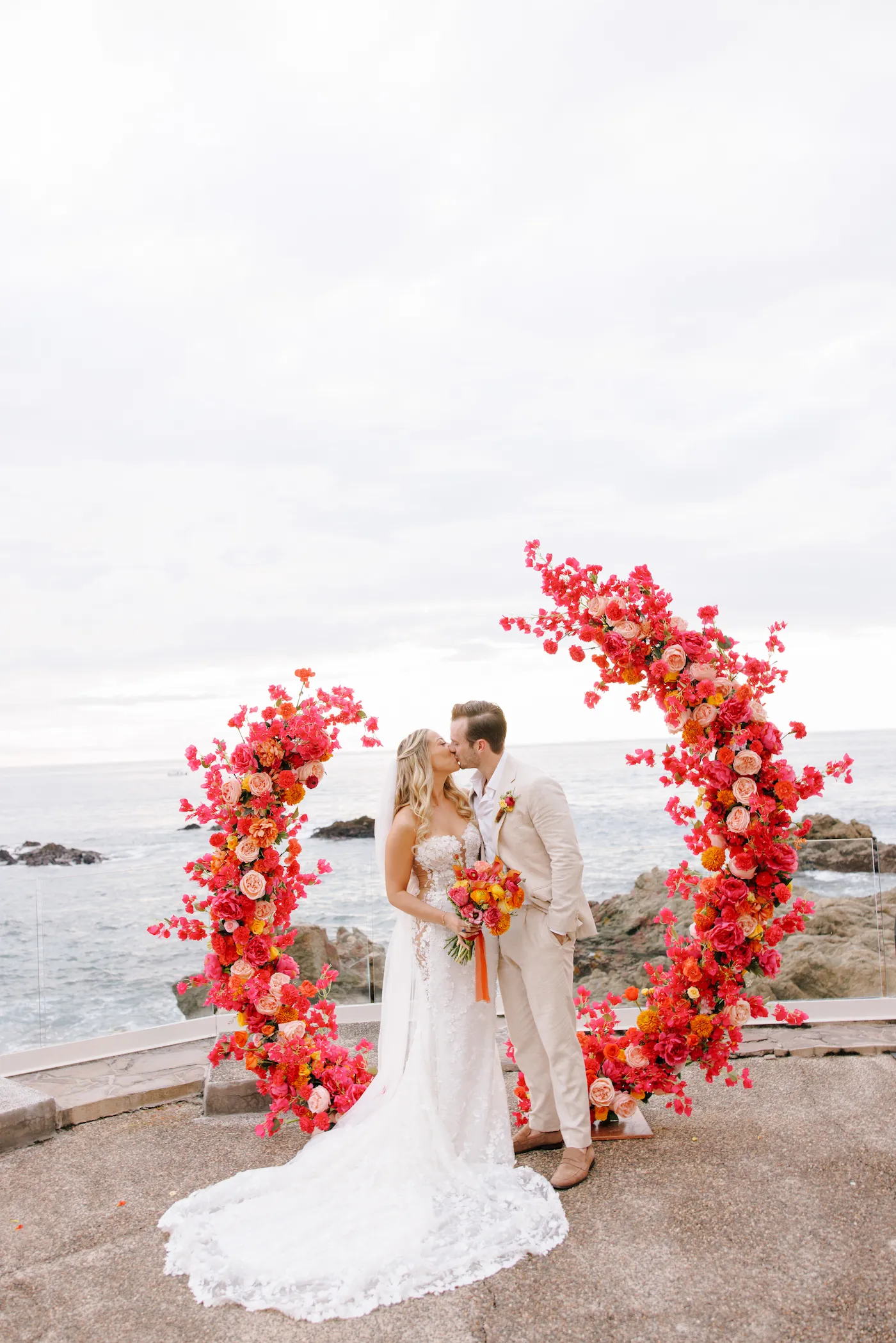 Raquel and Alex first kiss under vibrant red floral arch at Casa Karma Puerto Vallarta