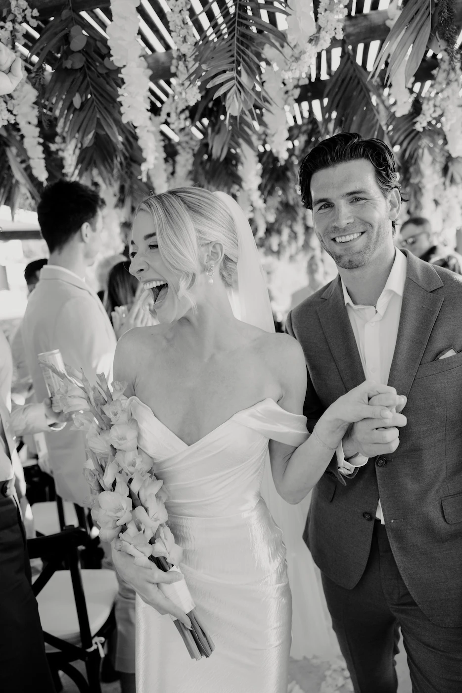 Bride and groom laughing together during wedding ceremony under tropical floral canopy Puerto Vallarta