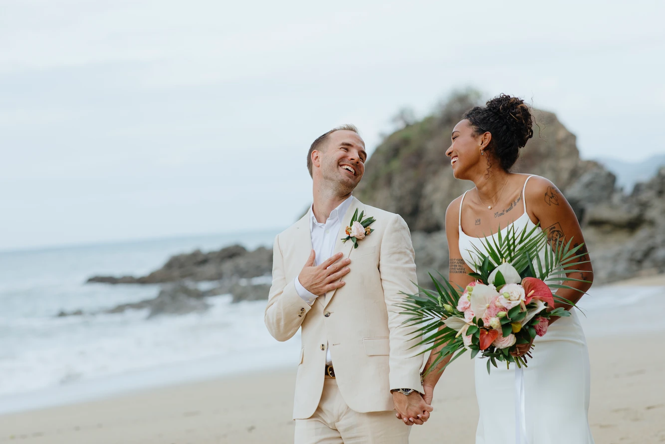 Wedding couple laughing on Sayulita beach with dramatic rock formation behind